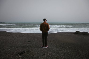 Sahilde dikilen genç bir adamın arka görüntüsü.