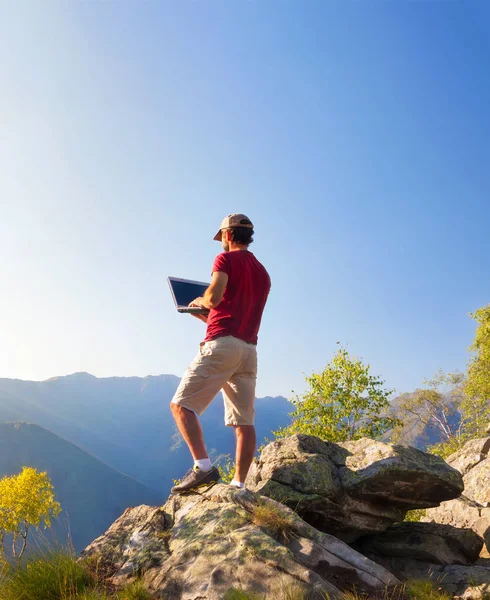 Человек, стоящий на скале и работающий на ноутбуке — стоковое фото