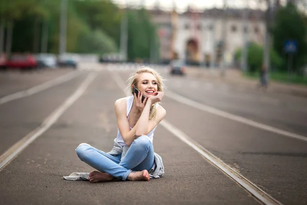 Gyönyörű lány ül az úton, és beszél a telefonon — Stock Fotó