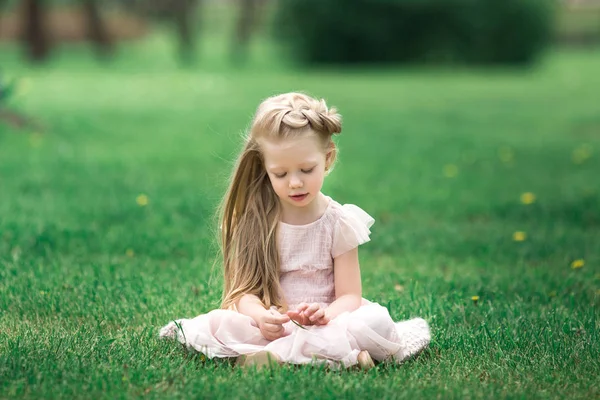 Little smiling girl sitting on the grass in the park — Stock Photo, Image