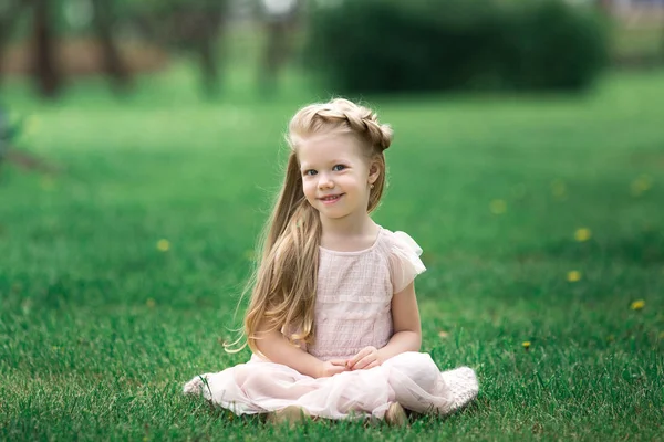 Pequena menina sorridente sentada na grama no parque — Fotografia de Stock