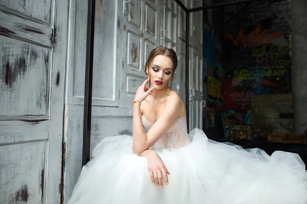 Mooie bruid met lichte make-up zit op het bed — Stockfoto