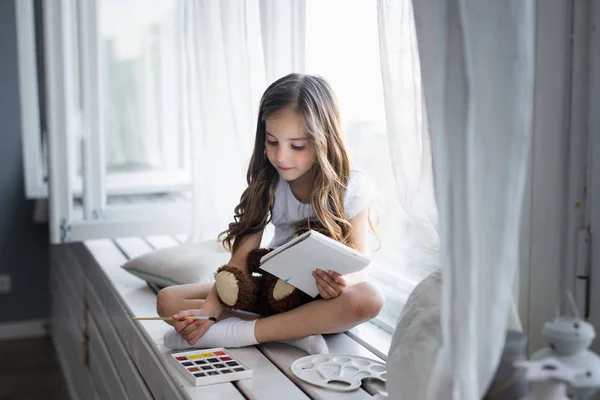 Beautiful girl draws paints on the window — Stock Photo, Image