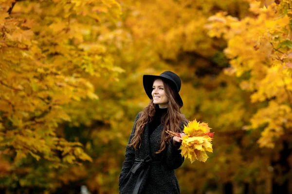 Женщина с осенними листьями в руке и осенью желтый кленовый сад фон — стоковое фото
