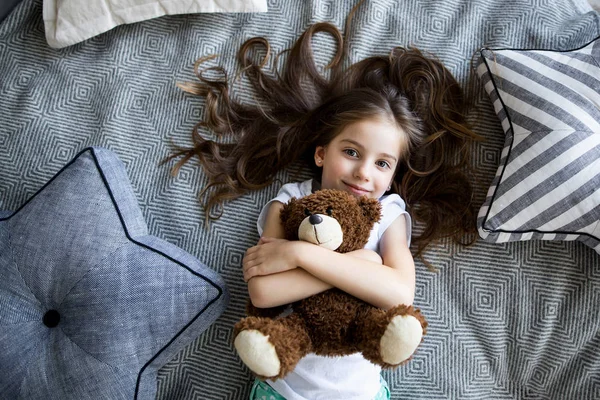 Niña está jugando con un oso de juguete en la cama — Foto de Stock