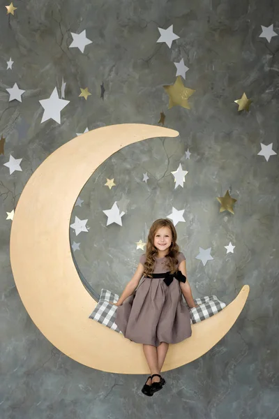 Маленькая девочка сидит на большой луне. Маленькая девочка мечтает — стоковое фото
