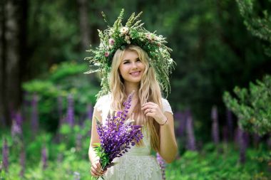 Beyaz elbise ve taze orman çiçek çelenk giyen ve mor çiçekler buket tutan güzel genç gelin portresi 