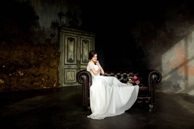 Gelin gibi karanlık studio iç kapalı sandalyede evde oturan beyaz elbiseli.