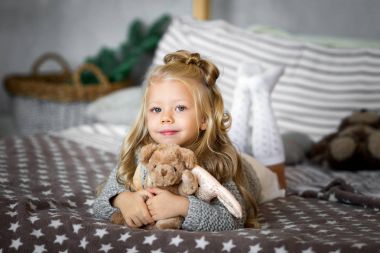 Sevimli küçük kız yatakta bir oyuncak ayı ile oynuyor