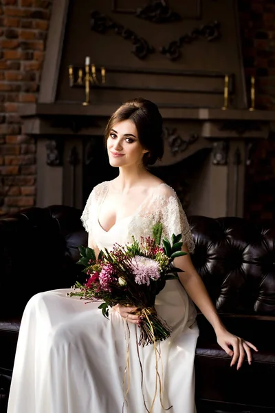 Bride in white dress sitting on chair indoors in dark studio interior like at home. — Stock Photo, Image