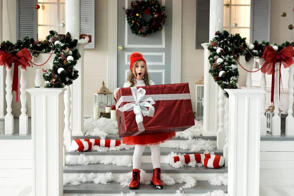 Glückliches Kleines Lächelndes Mädchen Mit Weihnachtsgeschenkbox Auf Der Veranda Des — Stockfoto