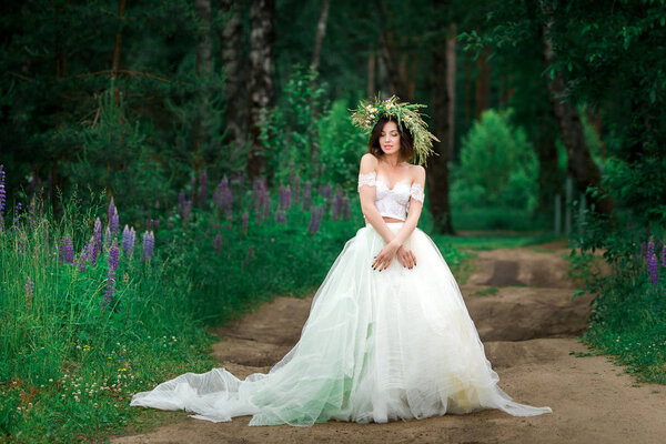 Portrait of beautiful young woman wearing white dress and wreath of fresh forest flowers