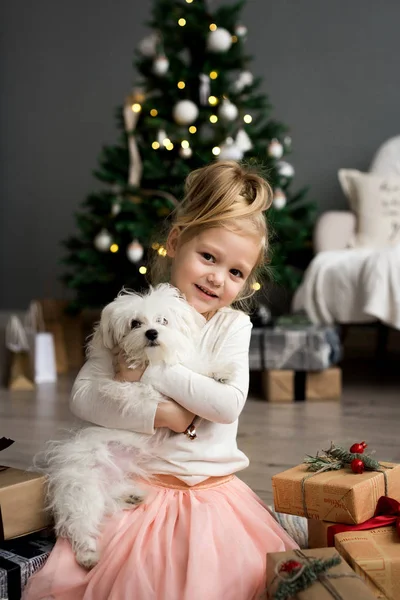 Hermosa chica con perro sentado cerca del árbol de Navidad. Feliz Navidad y Felices Fiestas . — Foto de Stock
