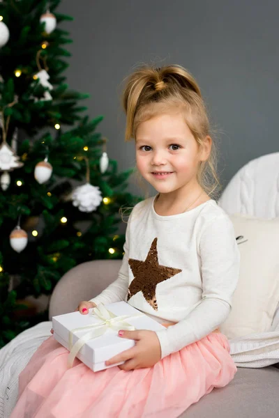 クリスマス ツリーに座ってギフト箱を持って幸せな笑みを浮かべて少女 — ストック写真