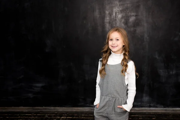 かわいい女の子が黒板と笑顔の黒の背景の上に立つ — ストック写真