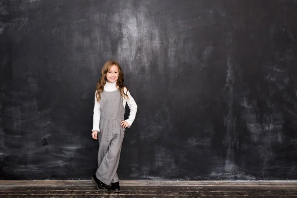 かわいい女の子が黒板と笑顔の黒の背景の上に立つ — ストック写真