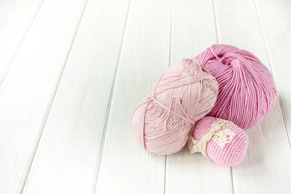 Light pink knitting yarn rolled into balls on a white wooden bac