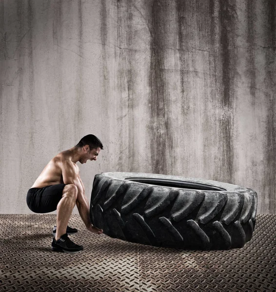 Homem muscular levantando um pneu grande — Fotografia de Stock