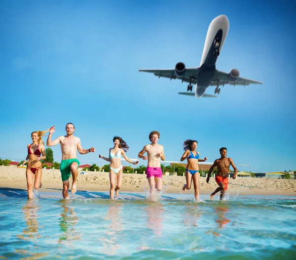 Grupo de amigos correm no mar com aeronaves no céu. Conceito de horário de verão — Fotografia de Stock