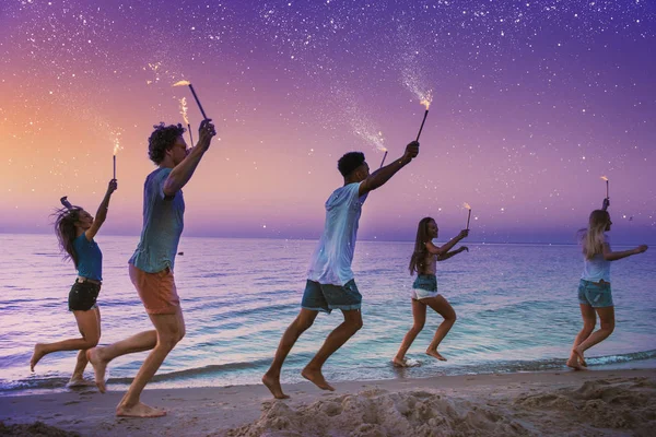 Gelukkige glimlachende vrienden rennend op het strand met sprankelende kaarsen — Stockfoto