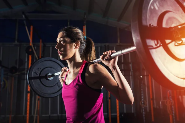 Menina atlética trabalha no ginásio com um barbell — Fotografia de Stock