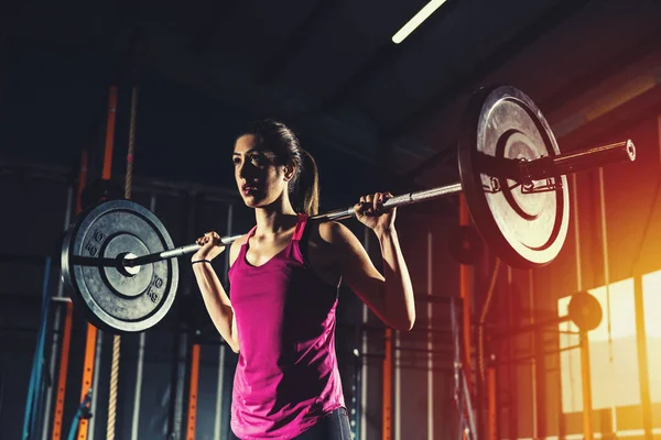 Menina atlética trabalha no ginásio com um barbell — Fotografia de Stock