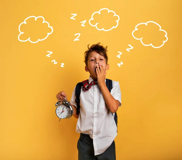 Jonge kind student met rinkelende wekker gaat lui naar school. Gele achtergrond. — Stockfoto