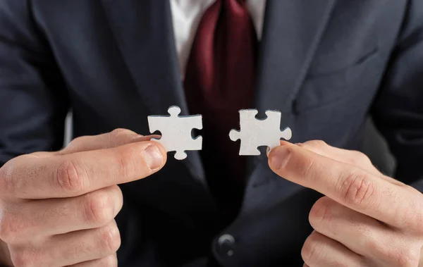 Zakenman sluit zich aan bij twee puzzelstukjes. concept van teamwork en partnerschap. — Stockfoto