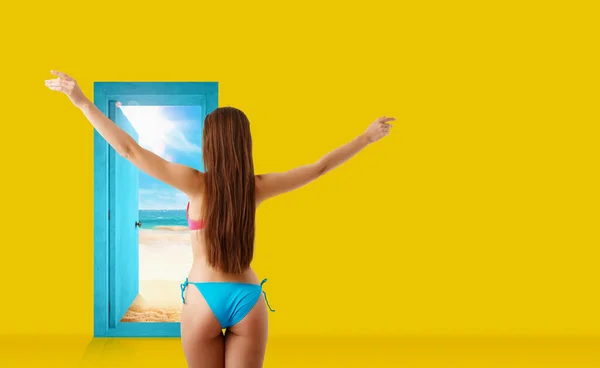Mädchen im Bikini geht durch eine Tür in der Wand an den Strand — Stockfoto
