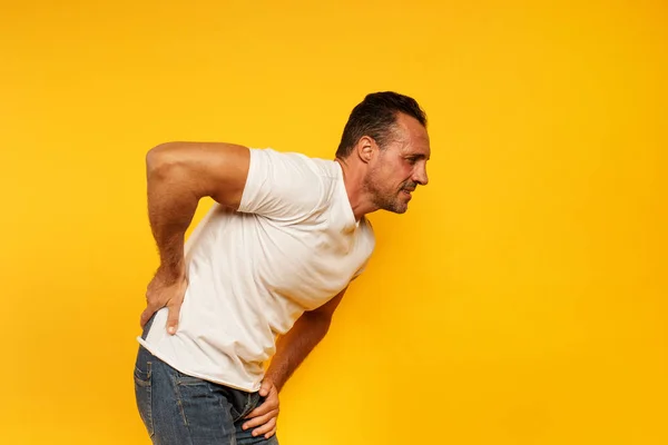背中の痛みを持つ男に達する。黄色の背景 — ストック写真