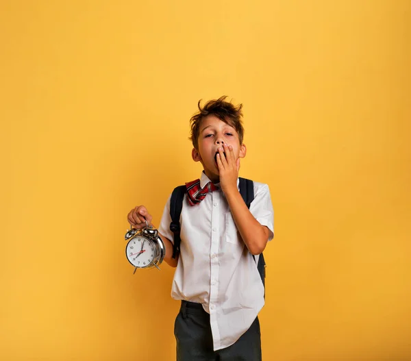 Çalan çalar saati olan genç bir çocuk okula gitmekte tembeldir. Sarı arkaplan. — Stok fotoğraf