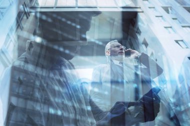 Senior businessman speaks on the mobile while walking in a modern city. Double exposure effect
