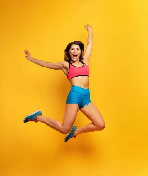 Sport kobieta skacze na żółtym tle. Szczęśliwa i radosna ekspresja. — Zdjęcie stockowe