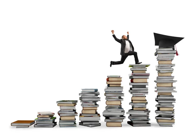 L'homme d'affaires atteint le chapeau de fin d'études sautant sur des piles de livres. Concept de réussite et de détermination dans l "étude — Photo