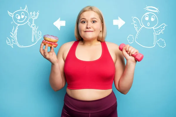 Fat girl pense à manger des beignets au lieu de faire de la gym. Concept d'indécision et de doute avec suggestion ange et diable — Photo