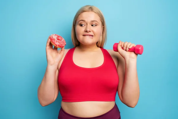 La cicciona pensa di mangiare ciambelle invece di fare ginnastica. Concetto di indecisione e dubbio — Foto Stock