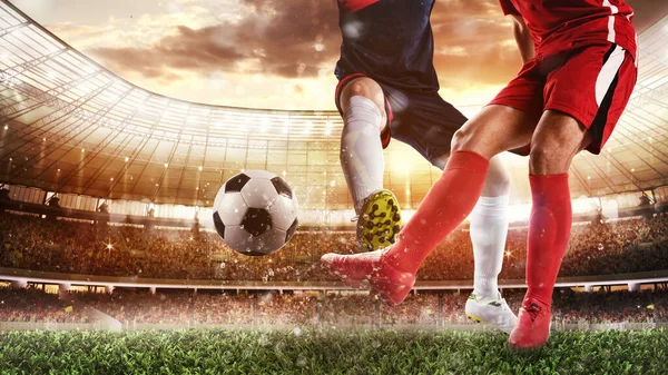 Escena de fútbol en el estadio con jugador en uniforme rojo pateando la pelota y oponente en tackle para defender —  Fotos de Stock
