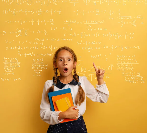 Young student is with shocked expression and indicates a complex formula. Yellow background — 图库照片