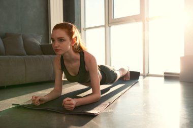 Genç kız güneş doğarken evde spor yapıyor.