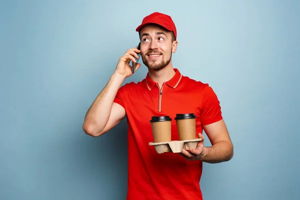 Kurier liefert heißen Kaffee und erhält Anruf am Telefon. Cyan-Hintergrund — Stockfoto