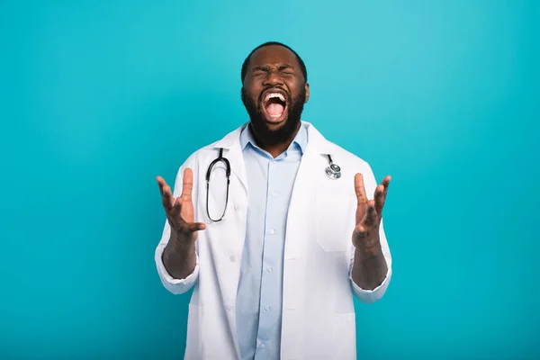 Médecin épuisé avec blouse de laboratoire et cris de stéthoscope sur fond cyan — Photo