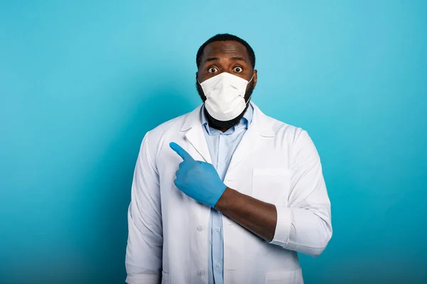 Besorgter Sanitäter mit Maske deutet etwas mit der Hand an. Blauer Hintergrund — Stockfoto