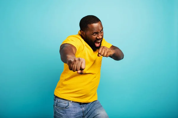 Man is angry and fights with punches. Blue background — Stock Photo, Image