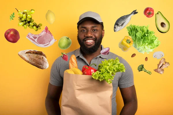 Deliveryman con espressione felice pronto a consegnare borsa con il cibo. sfondo giallo. — Foto Stock