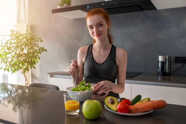 Spor elbiseli atletik kız mutfakta salata yiyor. — Stok fotoğraf