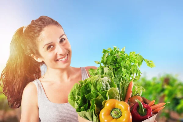 Девушка с сумкой, полной свежих овощей с огородом на заднем плане — стоковое фото