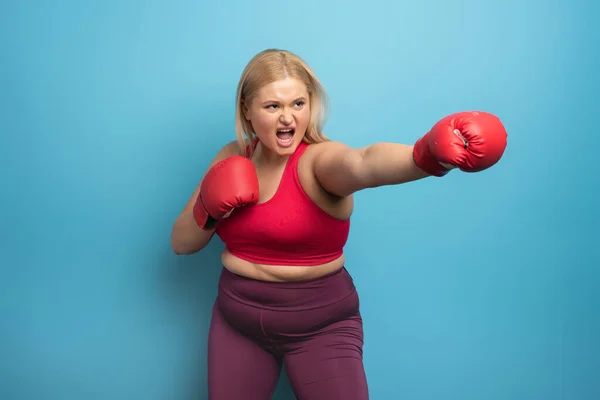 Fat girl in fitness suite does boxing. Cyan background
