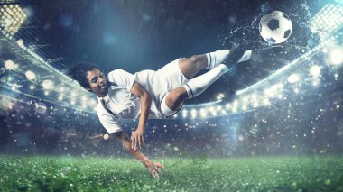 Futbolcu topa stadyumda havada akrobatik bir tekmeyle vuruyor.