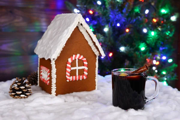 手作りのジンジャーブレッドハウス、雪の装飾、ホットワインと背景にガーランドと新年の木 — ストック写真
