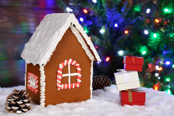 De handgemaakte eetbare peperkoek huis, sneeuw decoratie, geschenken en nieuwjaarsboom met slinger op de achtergrond — Stockfoto